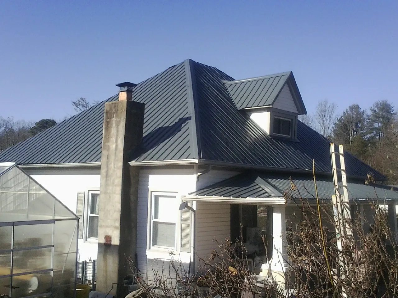 Dark blue standing seam metal roof on a white farmhouse with dormer — Slate & Tile Roof Repair by Roofing Brothers in Texas City