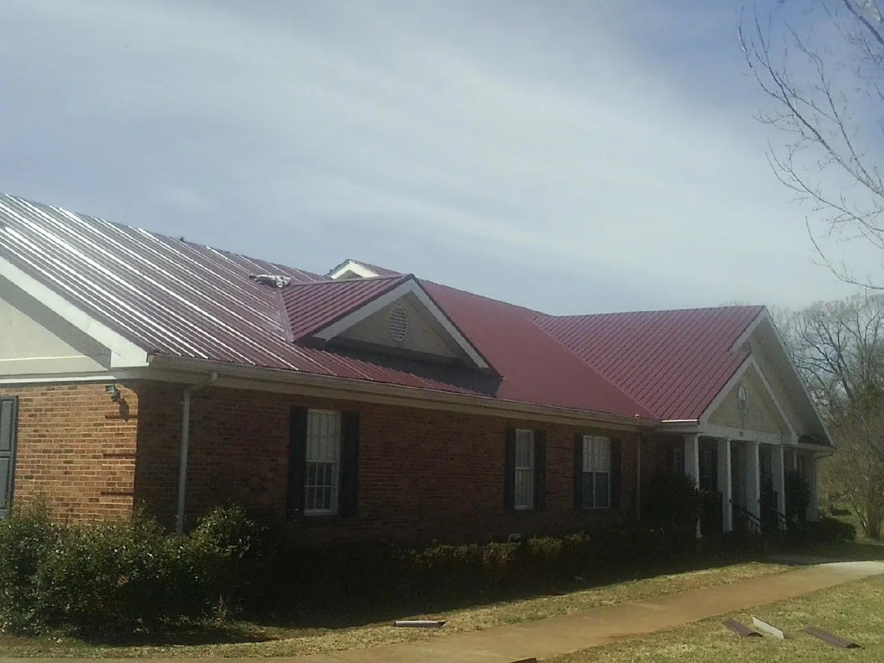 Red metal roof with gabled entries on a long brick building, from a Hail Damage Roof Repair job in Texas City