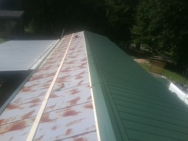 Old rusted panels beside newly installed green metal roofing — Wind Damage Roof Repair by Roofing Brothers in Texas City