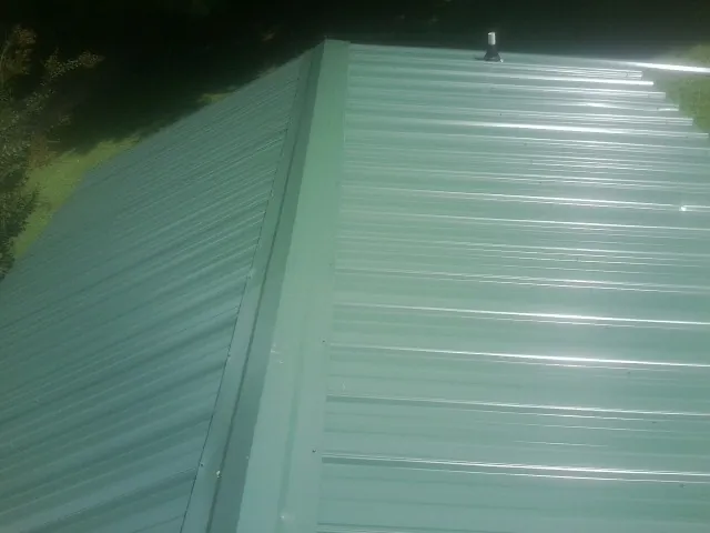 New green metal panels meeting at the ridge of a roof — Flat Roof Repair work by our crew in Texas City
