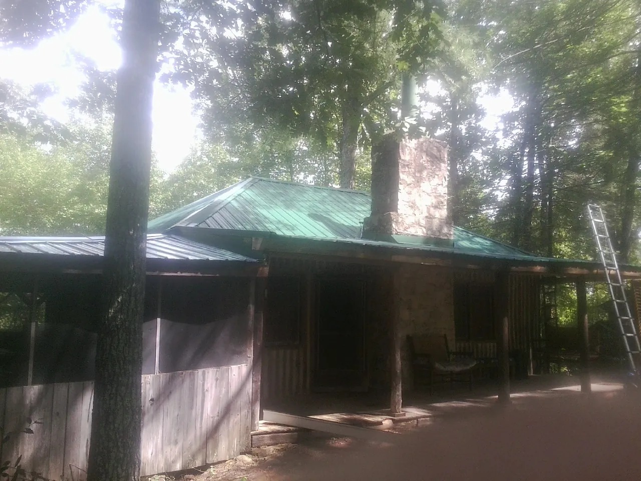Green metal roof and stone chimney above a log cabin porch in Texas City