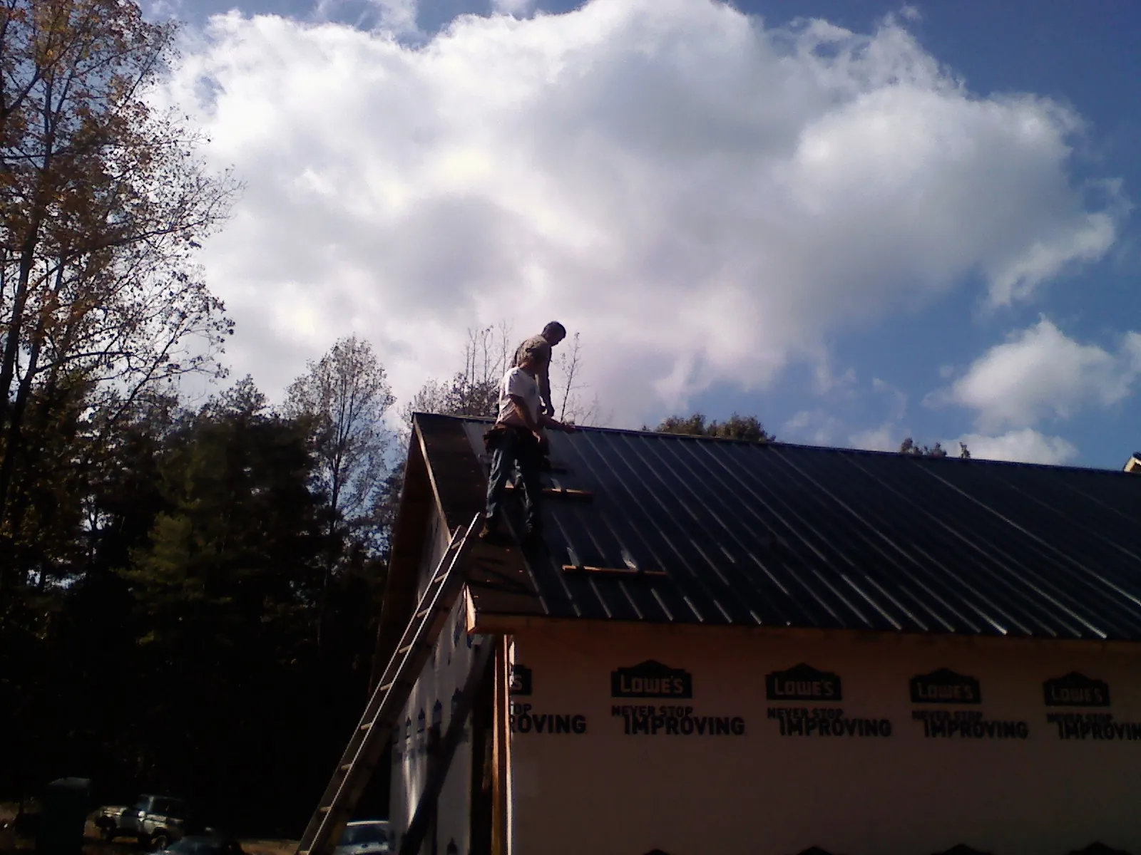 Roofer fastening dark metal panels high against a cloudy sky, from a Roof Inspection job in Texas City