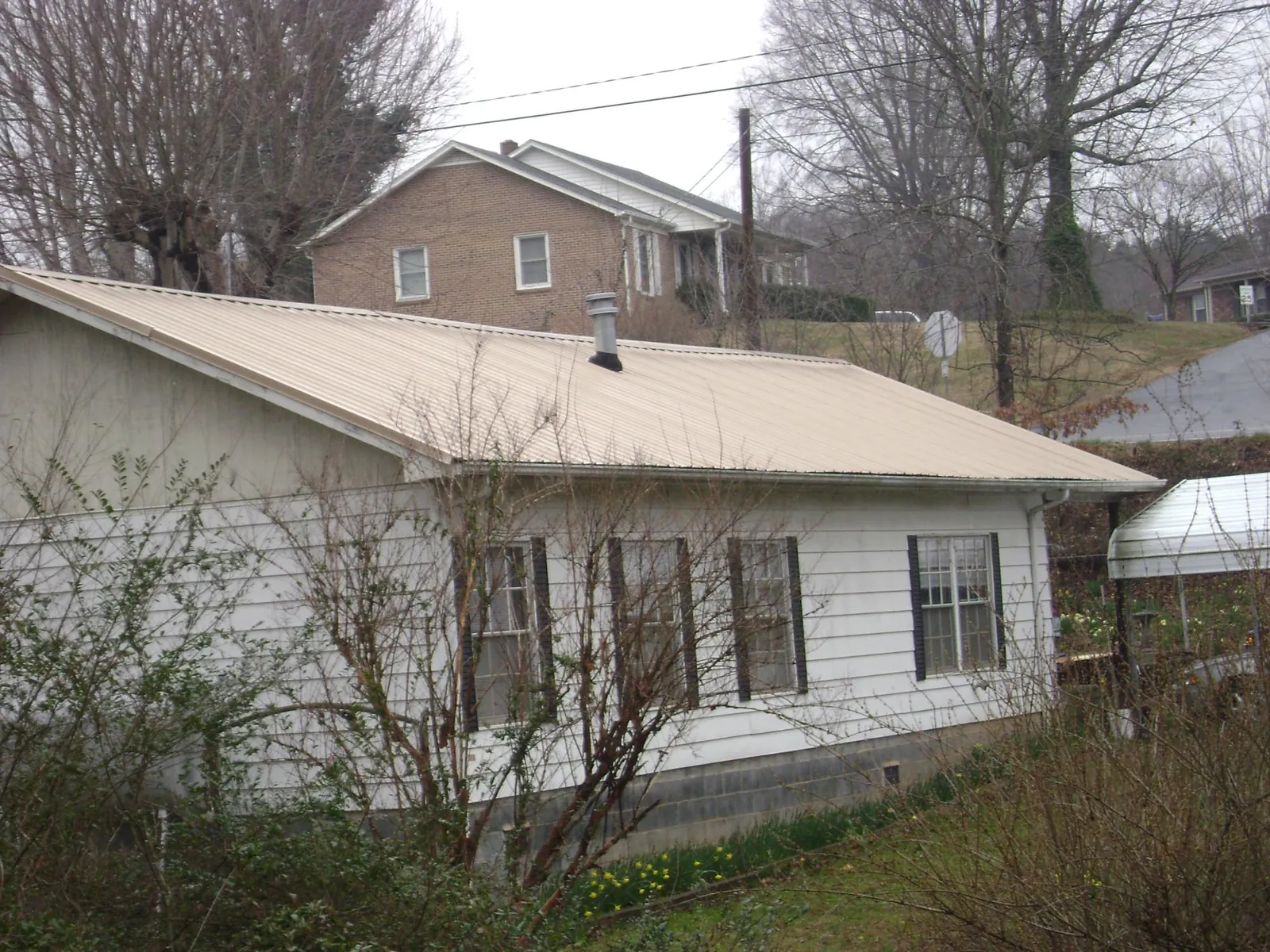 Tan metal roof on a white sided house set into a hillside — Commercial Roofing by Roofing Brothers in Texas City